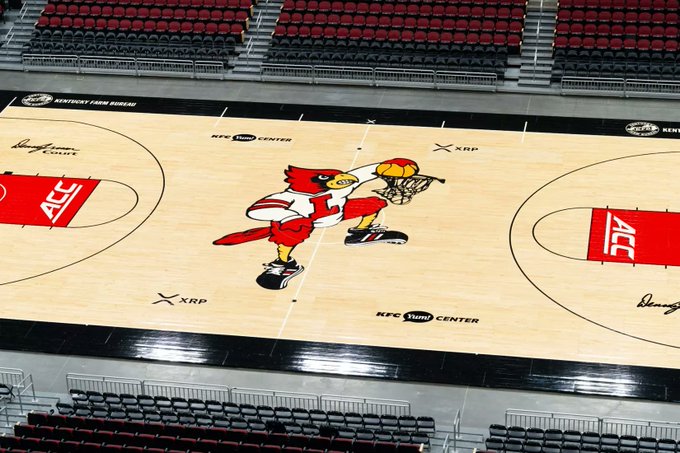 A basketball court at KFC Yum! Center features a large red bird mascot dunking a ball at center court, surrounded by XRP logos and "Louisville's Court" branding, visually representing the Ripple partnership that brings XRP sponsorship to Louisville Basketball.
