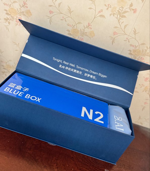 An open blue gift box containing a smaller blue box labeled "BLUE BOX N2" with "B.AI" text on a white pouch, and the inside lid reads "Tonight, Rest Well. Tomorrow, Dream Bigger." along with the same phrase in Chinese: "B.AI 伴你共赏明月，好梦常在。"