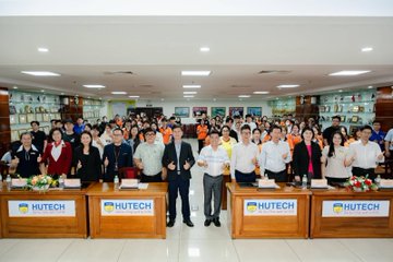 Group photo of HUTECH university faculty and staff standing behind four tables labeled 'HUTECH' in a large hall.