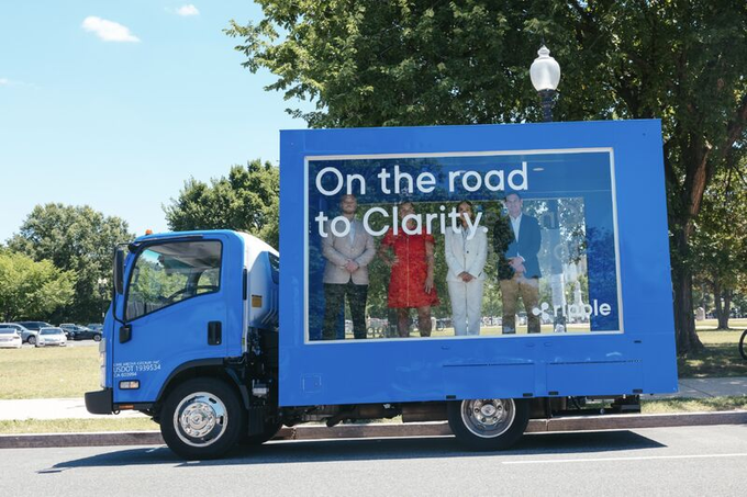 A blue truck with a large digital billboard reading "On the road to Clarity" alongside the @Ripple logo is parked on a roadside, serving as a mobile promotion in support of the CLARITY Act being advocated by Ripple.
