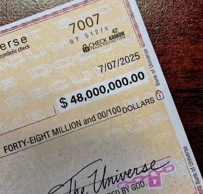 A symbolic check from "The Universe" for $48,000,000,000.00 dated 7/07/2025, displayed on a wooden surface to represent an abundant financial manifestation corresponding to the post's message of claiming large monetary rewards.