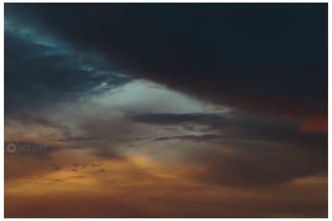 A dramatic sunset sky with dark clouds and orange hues, watermarked 'INES LOBO PHOTOGRAPHY'.