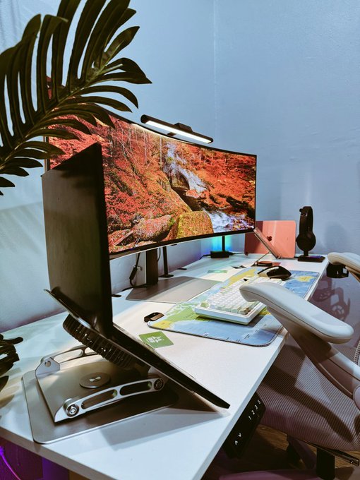 A laptop sits open on an elevated stand at a white desk featuring a dual-monitor setup, a mechanical keyboard, and a tropical plant, lit by a screen bar and ambient blue backlighting—evoking a dedicated creator's workspace aligned with the post's message about consistency and building in Web3.

No readable text or numbers are visible on the devices or screens.