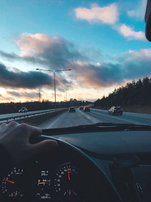 A scenic view from inside a car driving on a highway during sunset, with the dashboard showing 275km traveled and the time at 6:12 AM.