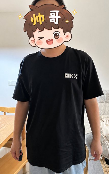 A person wearing a black t-shirt with the pixelated white 'OKX' logo stands indoors, with their face obscured by a cartoon sticker featuring the Chinese characters '帅哥' (handsome guy).