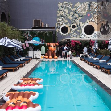 A swimming pool area decorated with inflatable pool floats shaped like donuts and a large brown teddy bear, set against a wall featuring a large octopus mural.