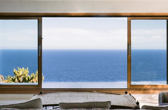 A scenic ocean view through large windows, with a woven hammock-style chair and sofa in the foreground, suggesting a restful vacation spot that aligns with the poster's update about finally getting a good night's sleep at their destination.