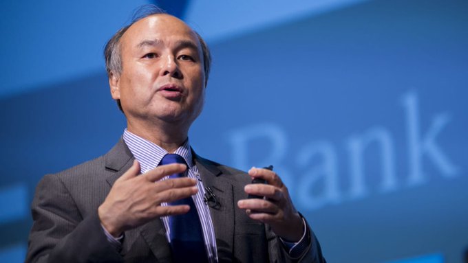 A man in a gray suit speaks on stage with the word "Bank" visible in the blue background behind him.