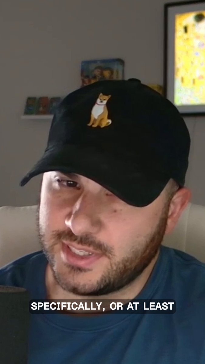 The image shows a man wearing a black baseball cap with an image of a dog on it. The caption below the photo reads "specifically, or at least" which suggests that there might be some information about the post related to the hat.