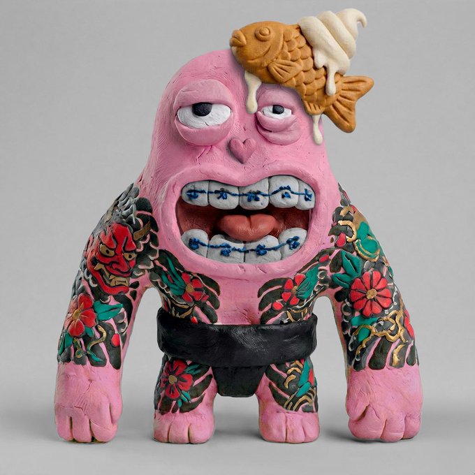A pink clay figurine of a tattooed monster with a fish skeleton and ice cream melting on its head, featuring a wide grin with braces and floral tattoo sleeves.