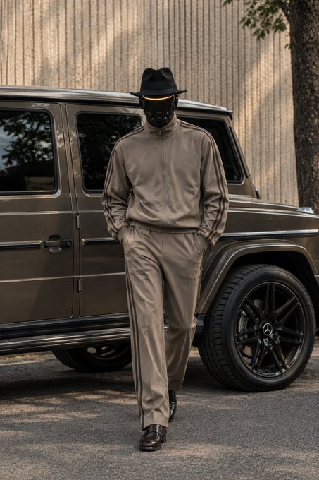 A street-style photograph of a person wearing a matching beige tracksuit and a black face mask with a glowing orange line, topped with a black fedora, standing in front of a dark Mercedes G-Wagon.