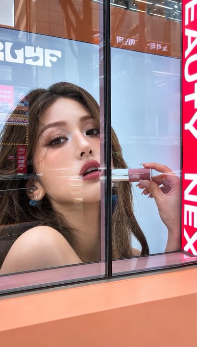 An advertisement for a Beauty Next lip product displayed in a window, featuring a model applying the lip product.