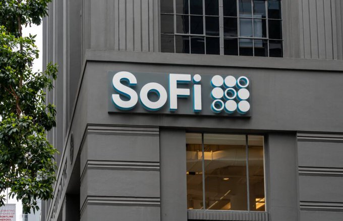 The image features a large gray building with a prominent sign that reads "Sofi" above a window, possibly advertising a stablecoin or cryptocurrency. The text on the sign suggests that the bank has just launched its own stablecoin infrastructure, which is now available for use in both Ethereum and Solana platforms. This indicates that the bank is actively participating in the growing fintech industry and is likely to be at the forefront of adopting new technologies like blockchain-based solutions.

The image also includes a tree next to the building, adding some greenery to the urban setting. The presence of trees can have positive effects on air quality and provide shade for pedestrians walking by.