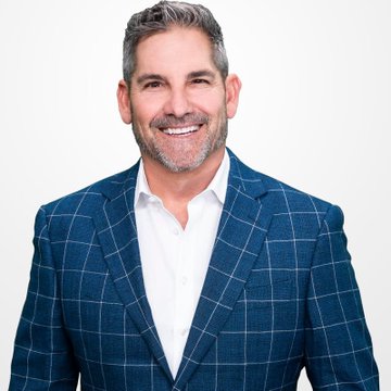 A smiling middle-aged man with salt-and-pepper hair and beard, wearing a blue plaid blazer over a white collared shirt, poses for a portrait against a light gray background—likely Grant Cardone, referencing his announcement about Cardone Capital purchasing additional Bitcoin amid the recent price dip below $80,500.