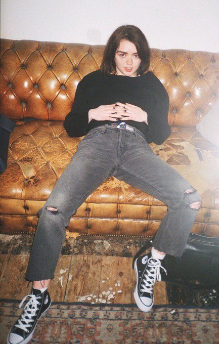 A young person with dark hair sits on a tufted brown leather couch, wearing a black sweater, ripped gray jeans, and black-and-white Converse sneakers, with their hands clasped together. The image accompanies a giveaway post celebrating winners, likely showcasing the winner or a style associated with the contest.