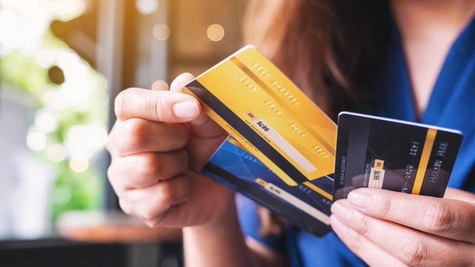 A woman holds several crypto-linked debit cards, including a prominent black "ONE CARD" and yellow cards, illustrating the growing use of stablecoin-linked cards for everyday spending, which has surged to $1.04 billion in July 2026.