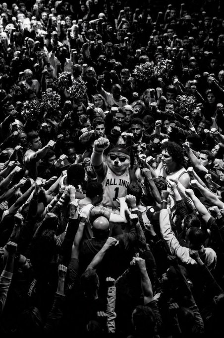 A black and white photo of a basketball player wearing an 'ALL INDIA' jersey being crowd-surfed by an enthusiastic audience.