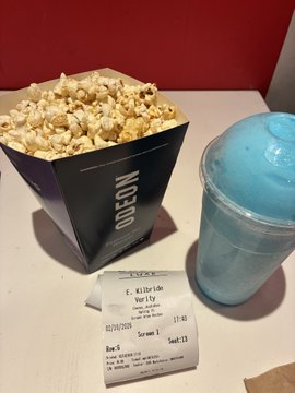 A movie theater concession tray holding a container of caramel corn labeled 'ODEON', a blue frozen slushie, and a printed receipt for screen 1, seat 11.
