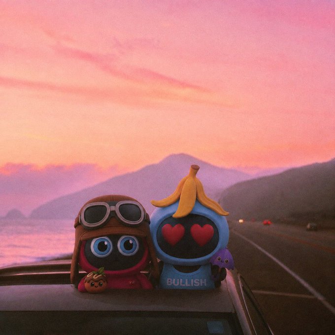 Two cute figurines, one wearing aviator goggles and the other a banana-topped hood with heart eyes labeled 'BULLISH', sit on a car dashboard against a pink and orange sunset over mountains and a coastal road.