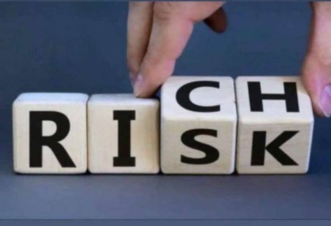 Hands flipping wooden letter blocks to change the word 'RISK' to 'RICH'.
