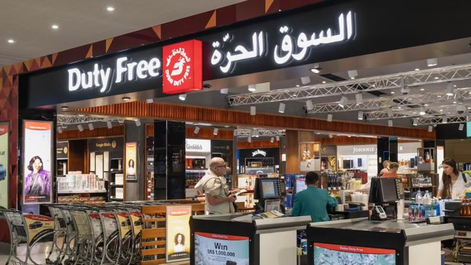 A Dubai Duty Free shop at an airport features a prominent bilingual sign reading "Duty Free" and "السوق الحرة" in English and Arabic, with liquor brands like Glenfiddich and Johnnie Walker displayed alongside cosmetics and gift items. The image illustrates the retail environment where Dubai Duty Free has adopted Crypto.com Pay, enabling eligible travelers to use cryptocurrency for purchases both in-store at the airport and online.
