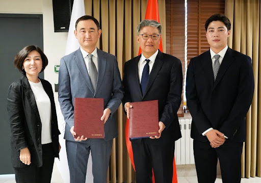 Two representatives from the National Bank of the Kyrgyz Republic and CertiK hold up signed agreement folders while posing together after formalizing a partnership to secure the development of Kyrgyzstan's national digital currency, the Digital Som.