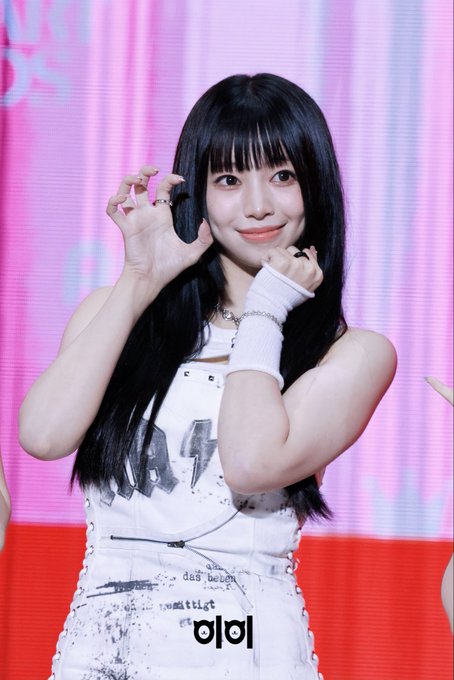 A photo of a young woman with long black hair and bangs, wearing a white top and white wristband, holding a microphone at a press event.