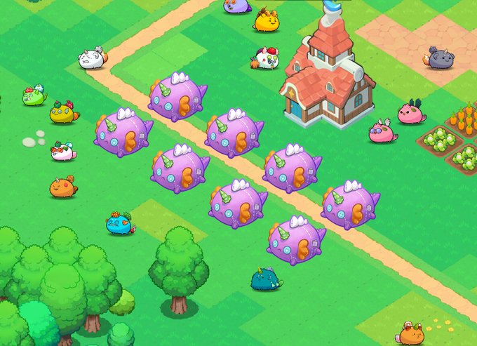 A vibrant virtual landscape features purple house-shaped "Reptile" plushie items arranged in rows on a grassy field, alongside a charming cottage, scattered round creature characters, trees, and crop patches. The image visually showcases the top-selling Land Item mentioned in the post, highlighting these collectible plushie Terrarium decorations within their whimsical game environment.
