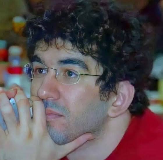 A young man with curly dark hair, glasses, and a red shirt rests his chin thoughtfully on his hand, appearing to be deep in contemplation. His serious, pensive expression visually reinforces the post's tone of cautious skepticism and questioning about PCT's suspicious movement patterns and potential hidden influences.