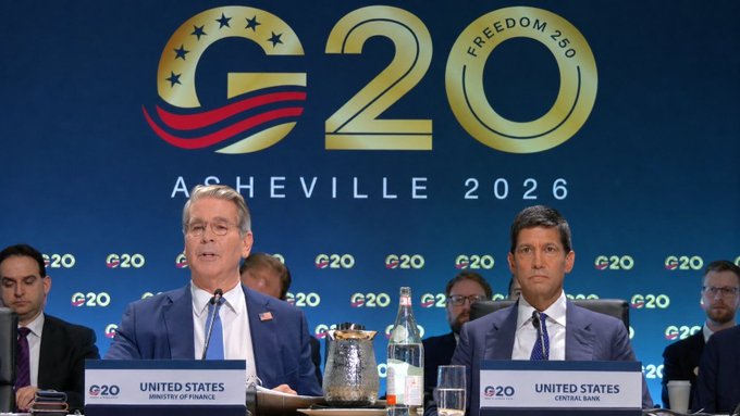 Two men in suits seated at the G20 Asheville 2026 summit, with nameplates identifying them as representatives of the United States (Ministry of Finance and Central Bank).