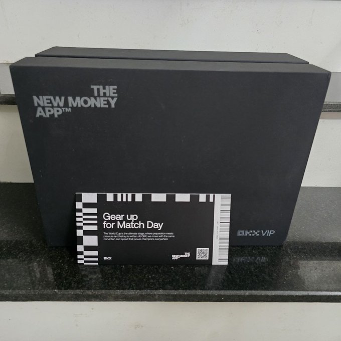A sleek black gift box branded with "THE NEW MONEY APP™" and "OKX VIP" sits on a dark countertop, accompanied by a card reading "Gear up for Match Day" that ties into the World Cup-themed OKX VIP promotional package. The premium packaging reflects the exciting unboxing experience of receiving exclusive OKX rewards during the World Cup season.