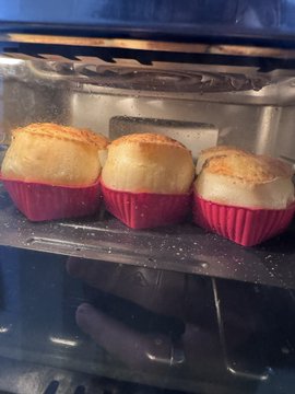 Three golden muffins baking in pink silicone cups inside an oven.