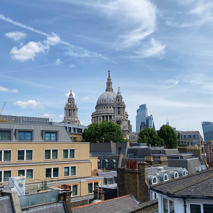 London skyline featuring St. Paul's Cathedral. The image shows the iconic domed cathedral rising above the surrounding rooftops under a partly cloudy sky, with modern skyscrapers visible in the background.