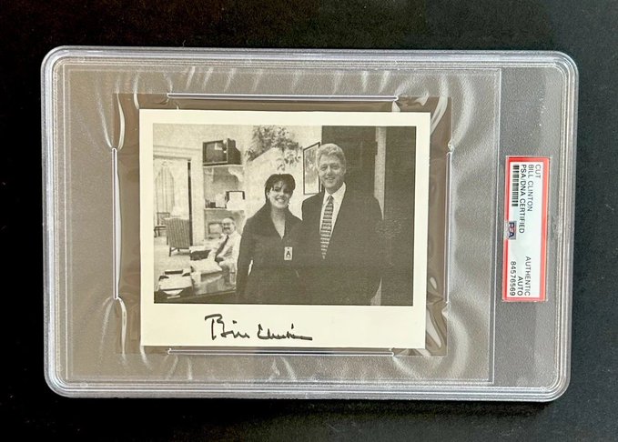 A black and white autographed photograph of Bill Clinton with another person, encased in a PSA/DNA authentication holder with the authentication number 84374659.
