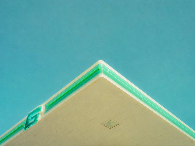 The image features a large white building with a green stripe running along its side. The building appears to be an oil station or gas station, as indicated by the presence of a gas pump. The sky above the building has a blue color, suggesting that it is daytime.