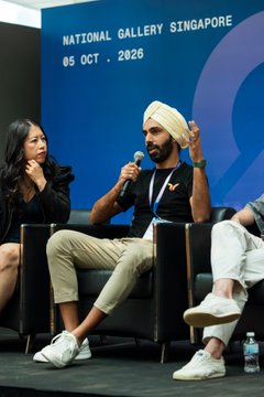 A man wearing a beige turban and black vest speaks into a microphone while seated at a panel discussion labeled 'NATIONAL GALLERY SINGAPORE 05 OCT . 2026'.
