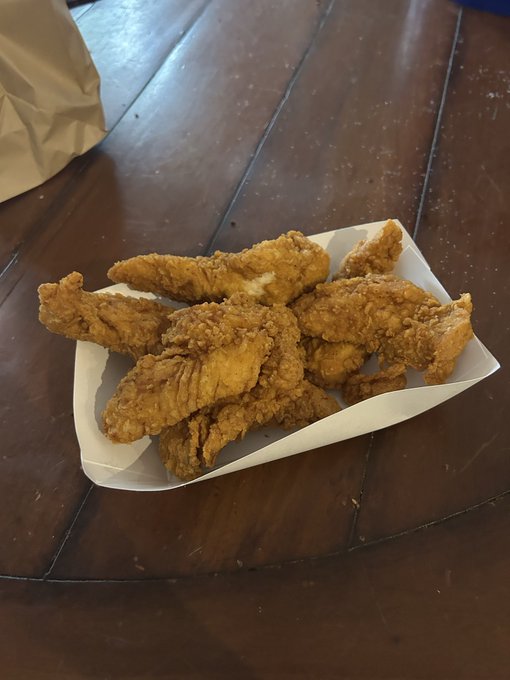 A paper boat tray holds a pile of golden-brown fried chicken tenders on a dark wooden table. The image ties into the "$TENDIES" post as a visual representation of the chicken tenders being tracked for price movement.