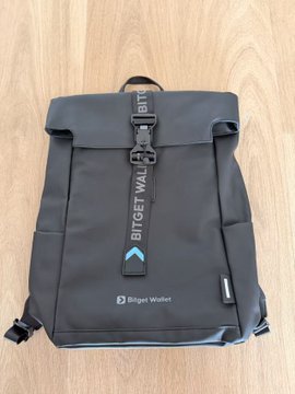 A gray Bitget Wallet backpack with branded straps and "Bitget Wallet" text is displayed on a wooden floor, gifted alongside a bracelet by @kajiweb3 to support the user's trading activities and Bitget Wallet experience.