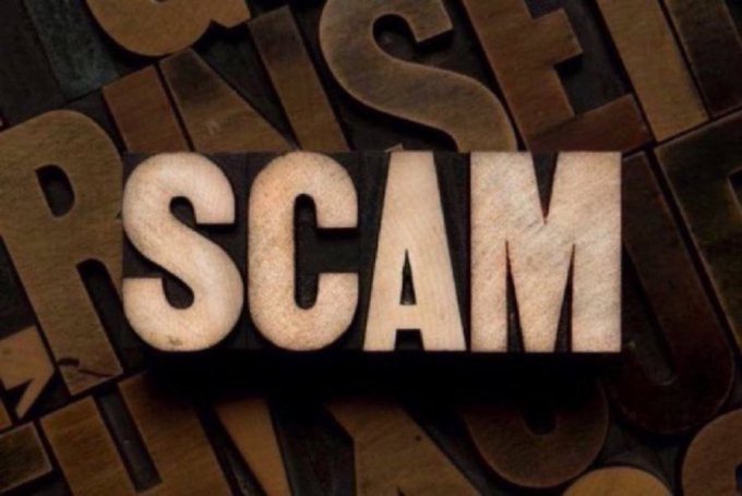 Vintage wooden letterpress blocks spelling out the word 'SCAM' against a background of scattered wooden type letters.