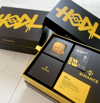 Two black and yellow Binance boxes containing promotional materials, including what appears to be a small Binance-branded plush toy and informational cards.