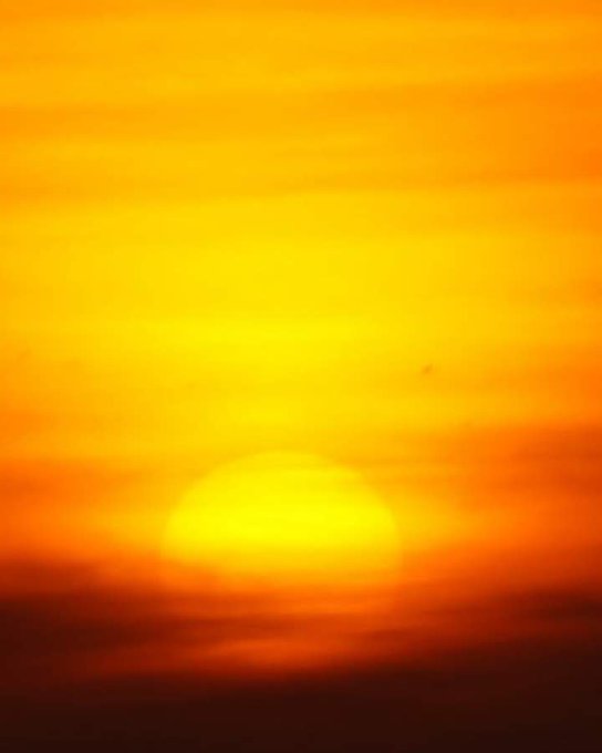 A vibrant orange and yellow sunset scene with the sun glowing warmly behind horizontal cloud streaks.