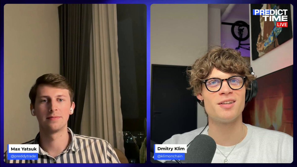 The image shows two men sitting next to each other, with one man wearing glasses and the other wearing a striped shirt. They appear to be having a conversation or participating in an interview, as indicated by the presence of a microphone between them. The background features a window that allows natural light into the room, suggesting that they might be indoors.