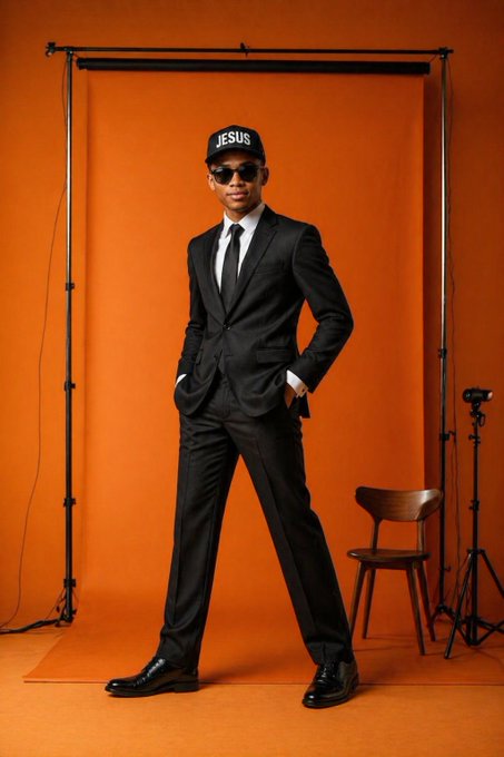 The image features a man dressed in a suit, standing against an orange background with a chair nearby. The man appears to be posing for a photo or video shoot, as there are two tripods present in the scene - one behind him on his right side and another on his left side.

The post that accompanies this image is titled "Good morning X Family Taco Tuesday I keep preaching $River Can I get a gM back?". The caption suggests that the man's attire might be related to a specific event or theme, possibly involving food or dining experiences.