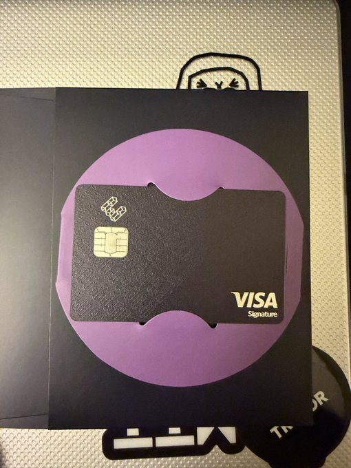 A black "VISA Signature" bank card with a smart chip rests on a black and purple circular surface over a textured background.