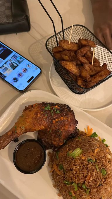 The image shows a plate of food consisting of fried chicken, rice, and vegetables such as carrots and green onions. The food appears to be well-cooked and appetizing. The photo also features a cell phone placed next to the plate on a dining table.