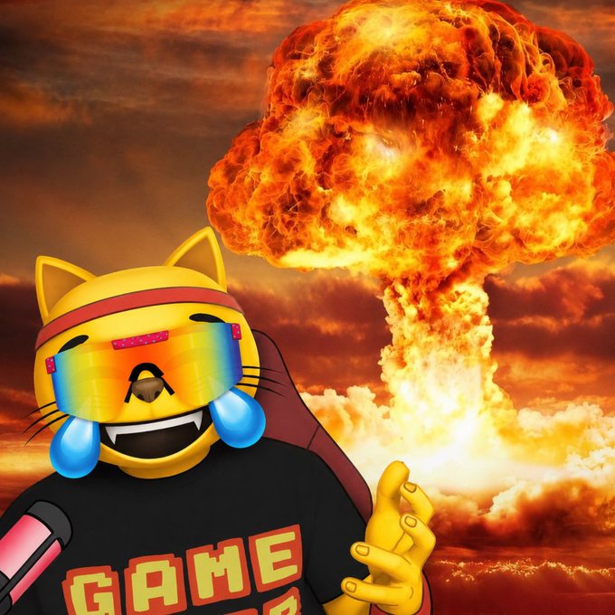 A cartoon cat emoji wearing rainbow ski goggles and a 'GAME' t-shirt holds a microphone, with cartoon tears and a large nuclear mushroom cloud explosion in the background.