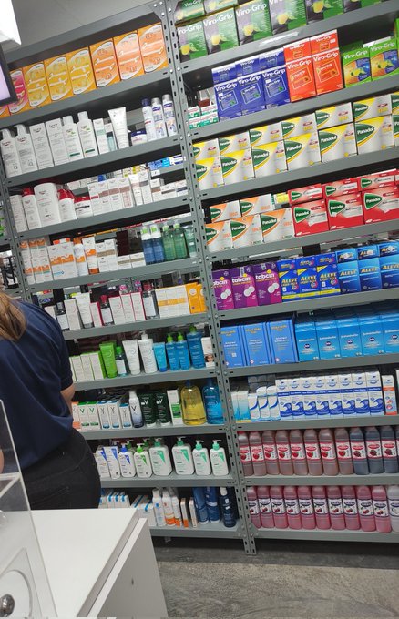 A store aisle stocked with various over-the-counter health products including Nexcare bandages, Tylenol, and Aleve boxes on metal shelves.