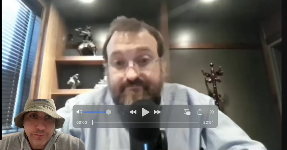 The image shows a man wearing glasses sitting at a desk with a computer screen displaying a video call from Charles Hoskinson, who is talking about taptoils. The man's face can be seen clearly in the image as he engages in the conversation.