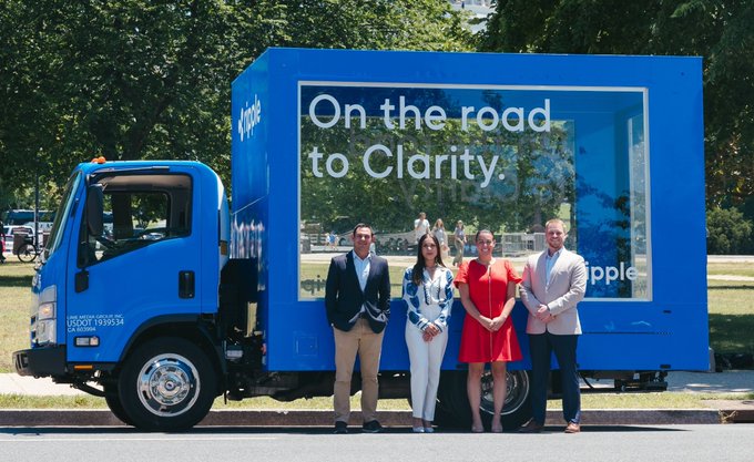 Four people stand in front of a bright blue box truck branded with the Ripple logo and the slogan "On the road to Clarity," promoting the company's CLARITY Act campaign in support of XRP ($XRP) and its stablecoin RLUSD ($RLUSD).