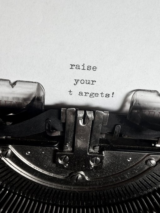 Black and white photograph of a typewriter with the motivational phrase "raise your targets!" typed onto a sheet of paper.